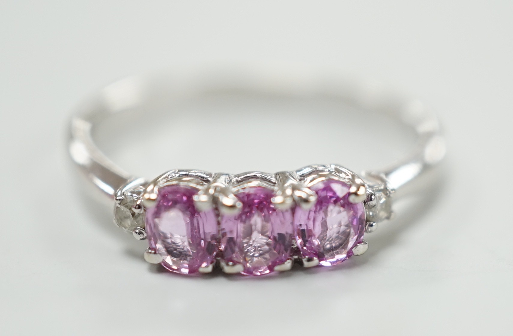 A modern 14ct white gold, three stone pink sapphire and two stone diamond chip set ring, size L, gross weight 1.5 grams.